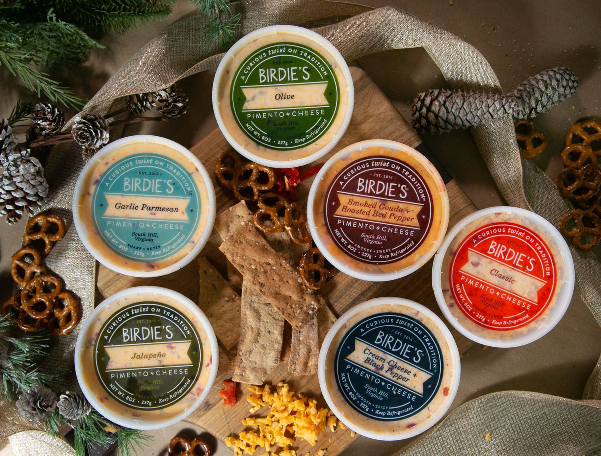 Six flavors of Birdie's Pimento Cheese with pretzels, crackers and pine cones