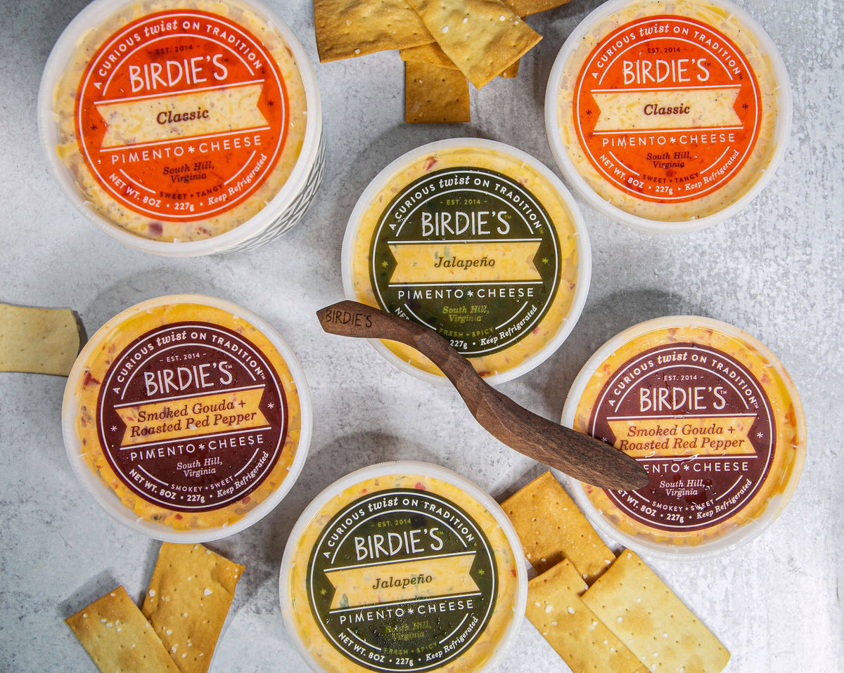 Tubs of Birdie's Classic, Jalapeño and Smoked Gouda + Roasted Red Pepper pimento cheese with crackers and a wooden spreader