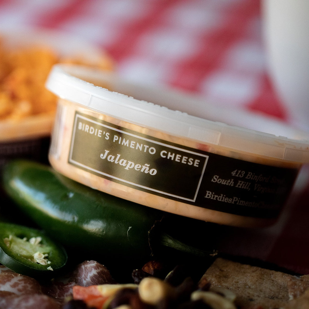 Tub of Birdie's Jalapeño pimento cheese with fresh jalapeños on a charcuterie board