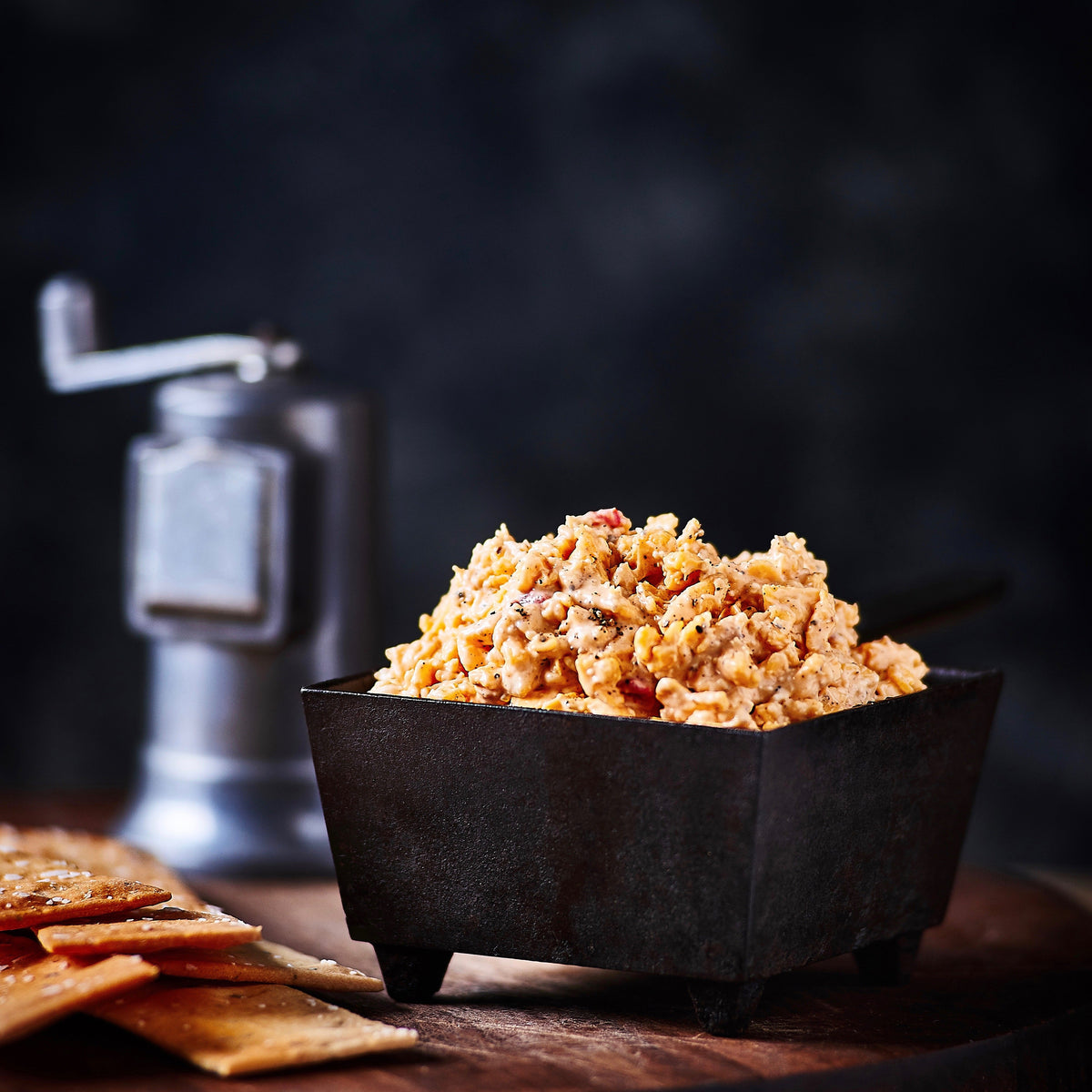 Birdie's Cream Cheese + Black Pepper pimento cheese in a black bowl with crackers and a pepper mill